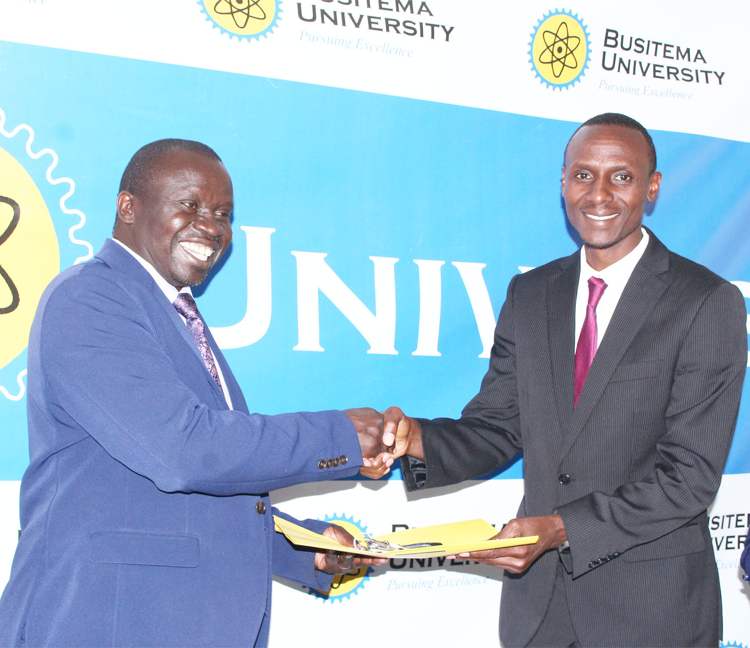 The Vice Chancellor symbolically hands over a file to Dr. Gregory Tweheyo, signifying his official assumption of office.